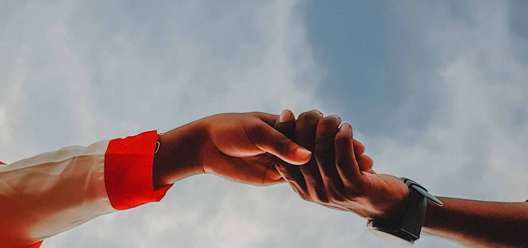 Two people clasping hands against a cloudy sky