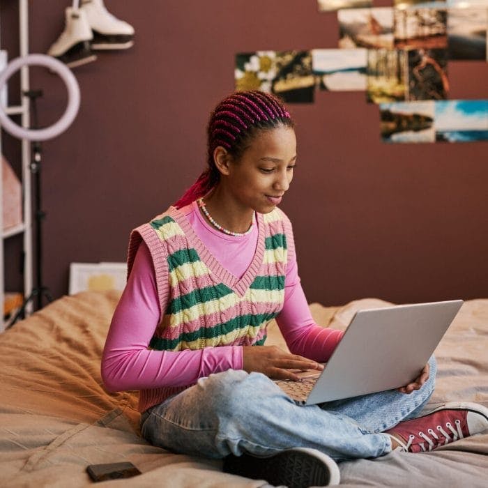 young girl sits on a bed with a laptop