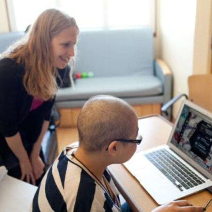 cancer patient plays re-mission on laptop while adult looks on