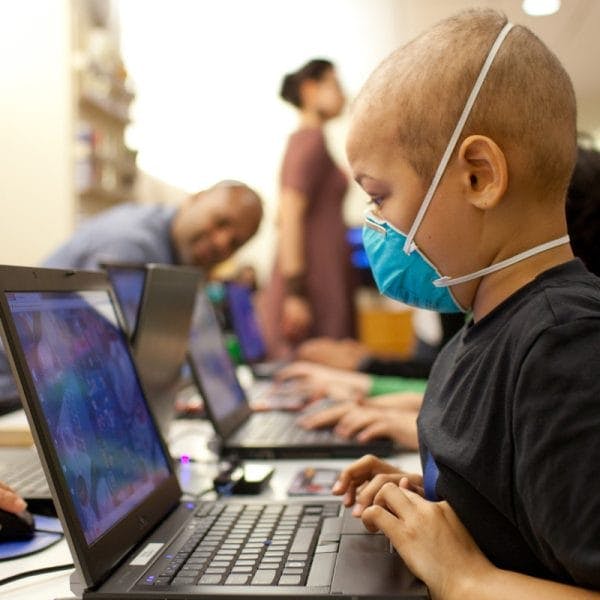 child wearing a blue mask looks at a laptop computer
