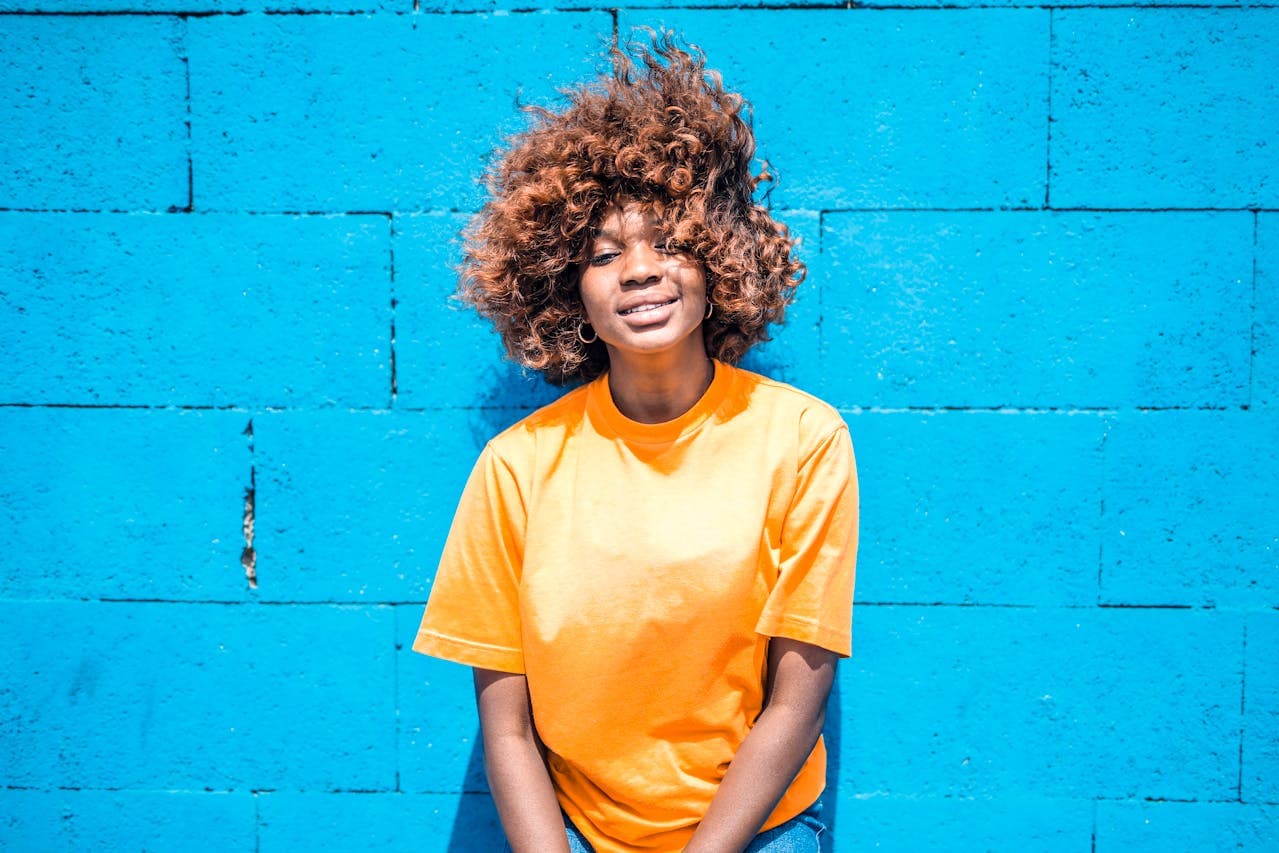 Photo of Smiling Woman in Orange T-shirt Leaning on Blue Wall