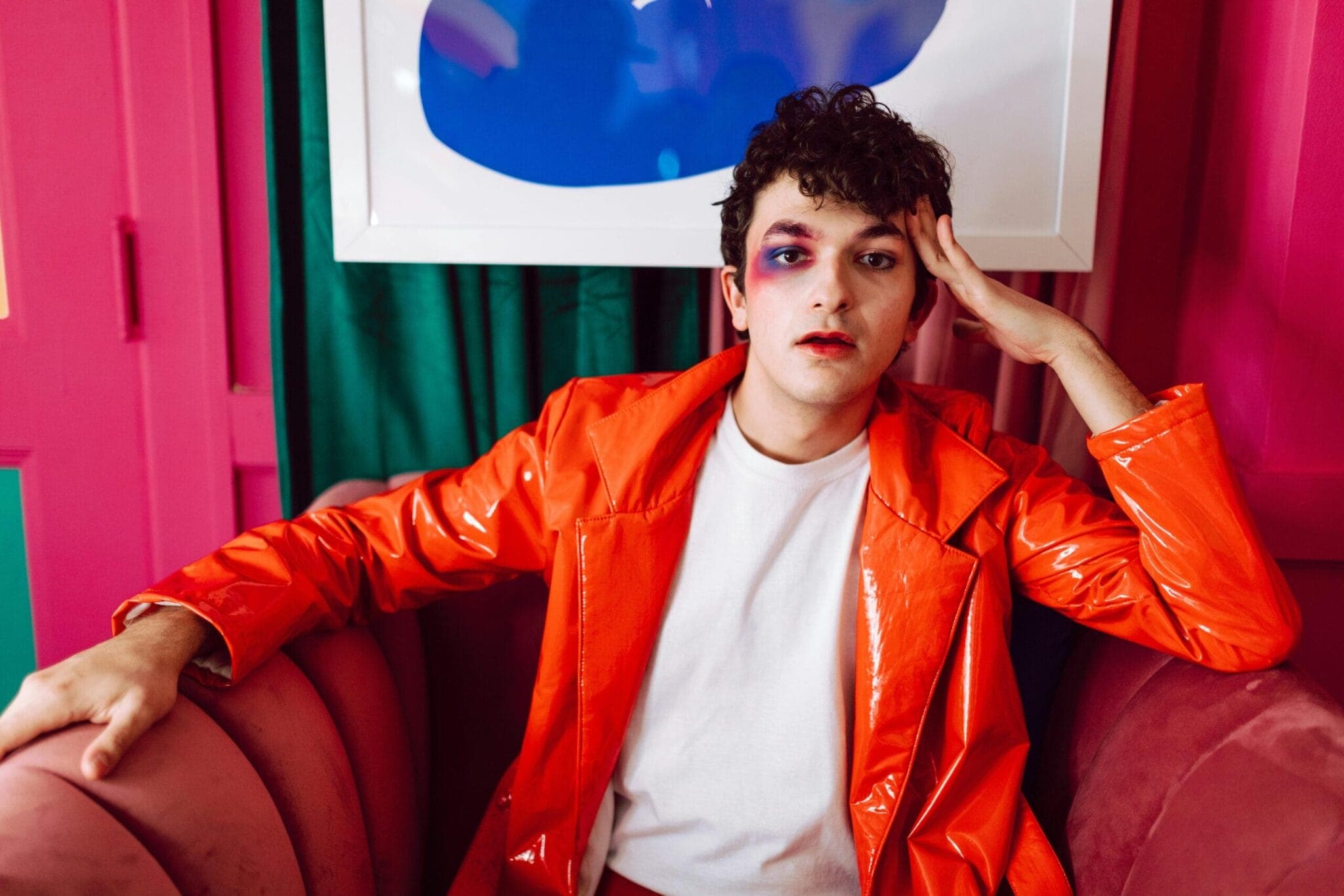 A close-up portrait of a person with bold, colorful makeup and an avant-garde fashion style