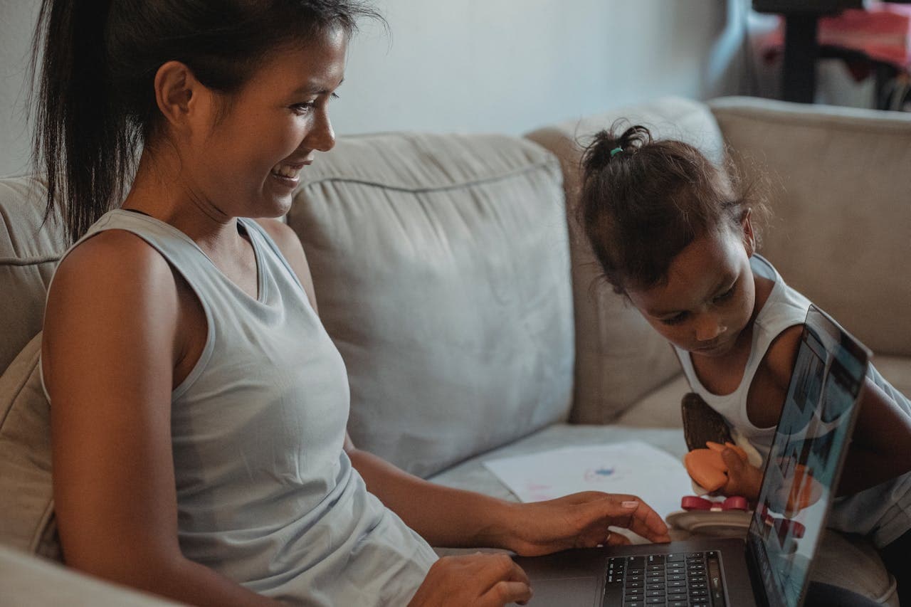 Hispanic mother and daughter using laptop on sofa